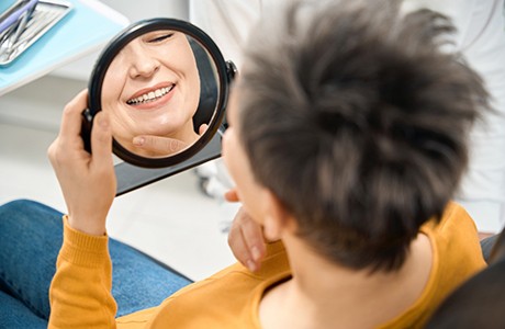 Happy dental patient admiring her smile in mirror