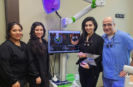 Dentist and three team members smiling next to computer showing digital models of a jawbone