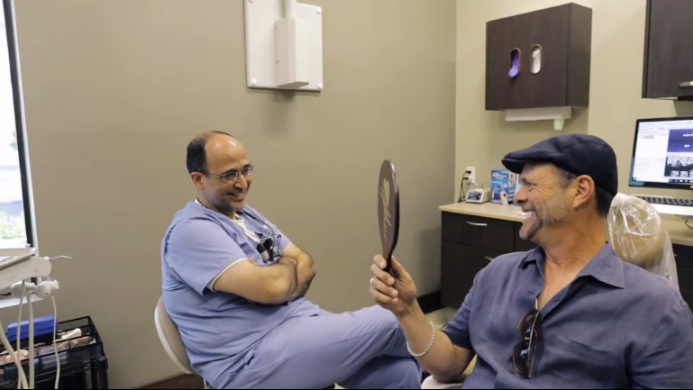 Doctor Iskandar smiling as a dental patient looks at his teeth in a mirror