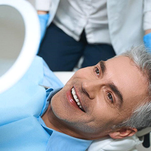 Senior man lying back in dental chair and looking at smile in mirror