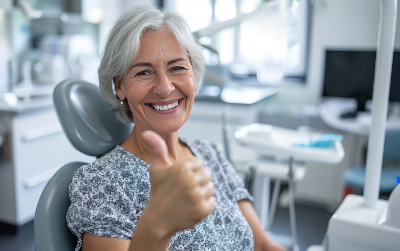 an older woman giving a thumbs up in the dentist’s office